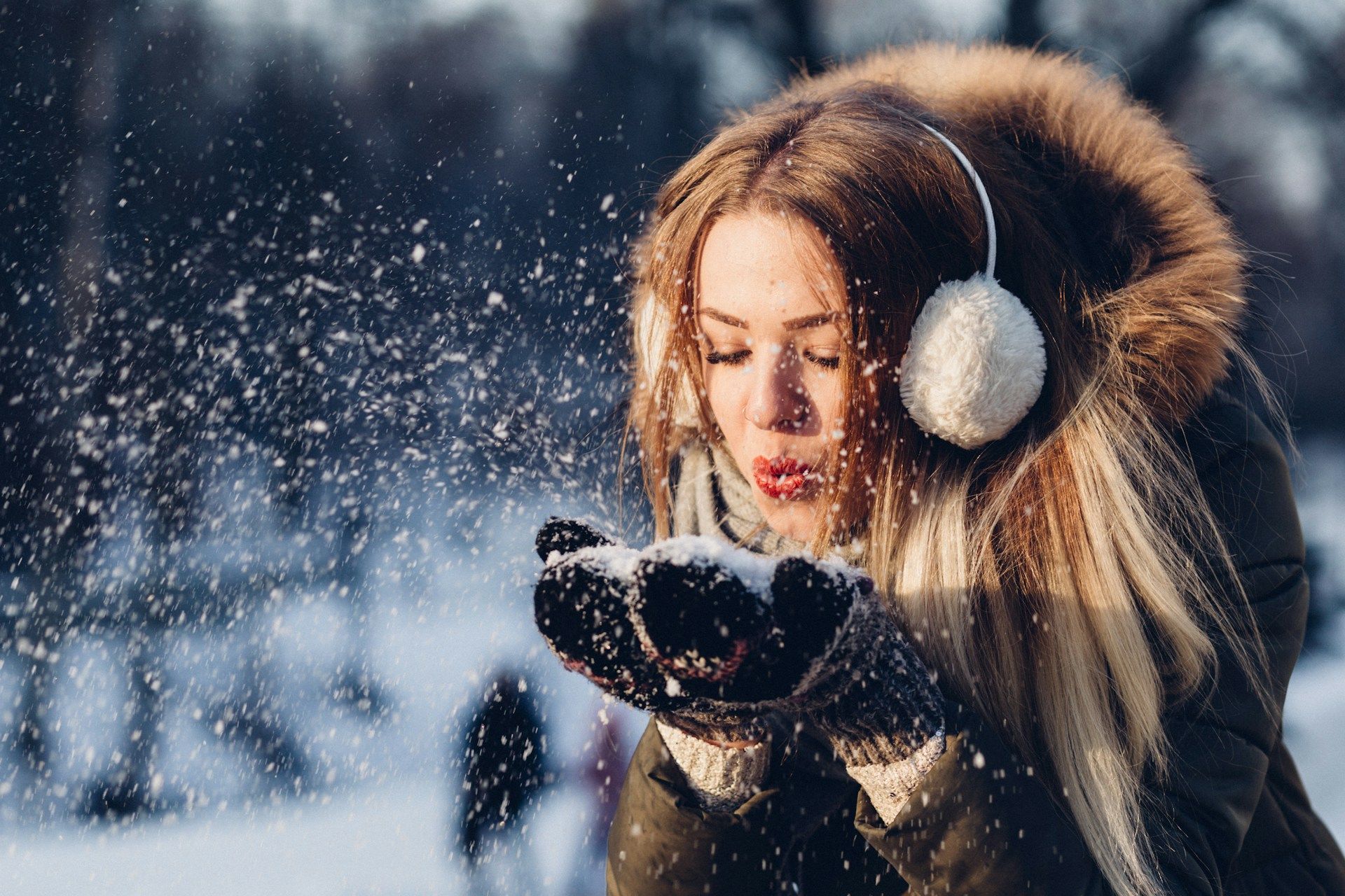 Dziewczyna w parku zimą zdmuchuje śnieg z rękawiczek
