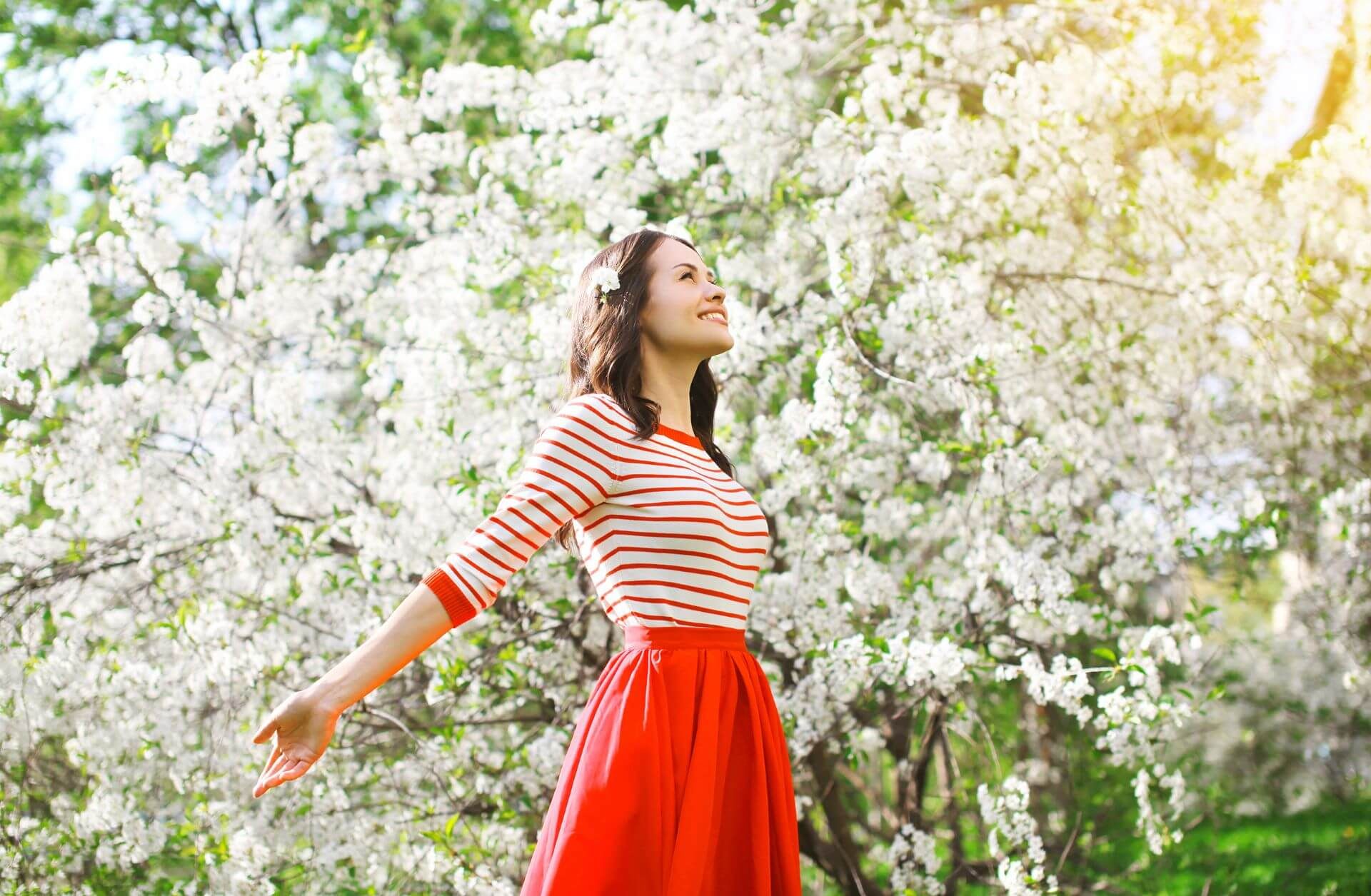 młoda kobieta w czerwonej spódnicy na tle kwitnącego wiosennego drzewa