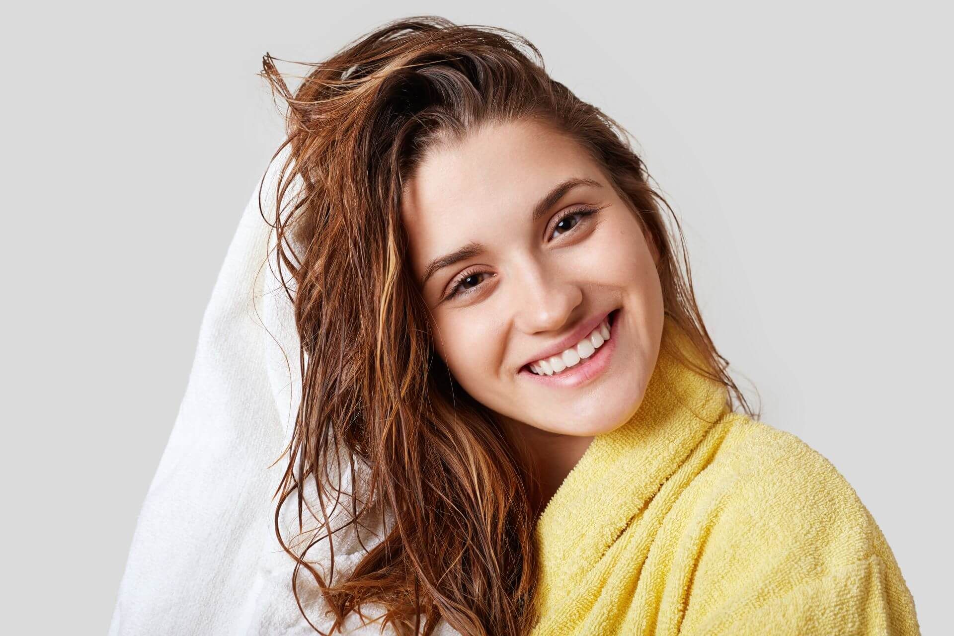 Młoda usmiechnięta kobieta wyciera mokre włosy ręcznikiem