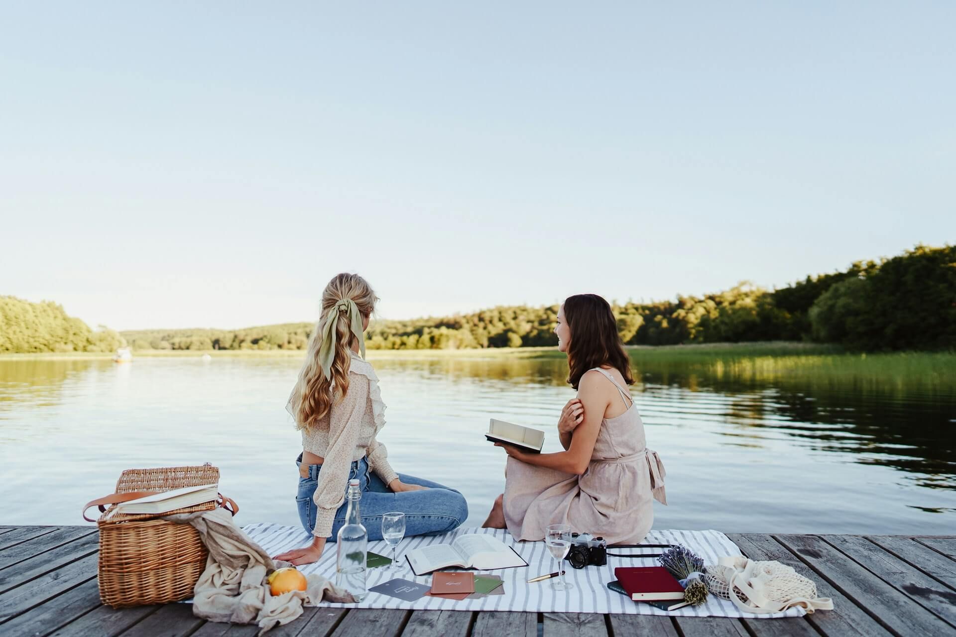 Dwie kobiety siedzą na kocu piknikowym nad wodą