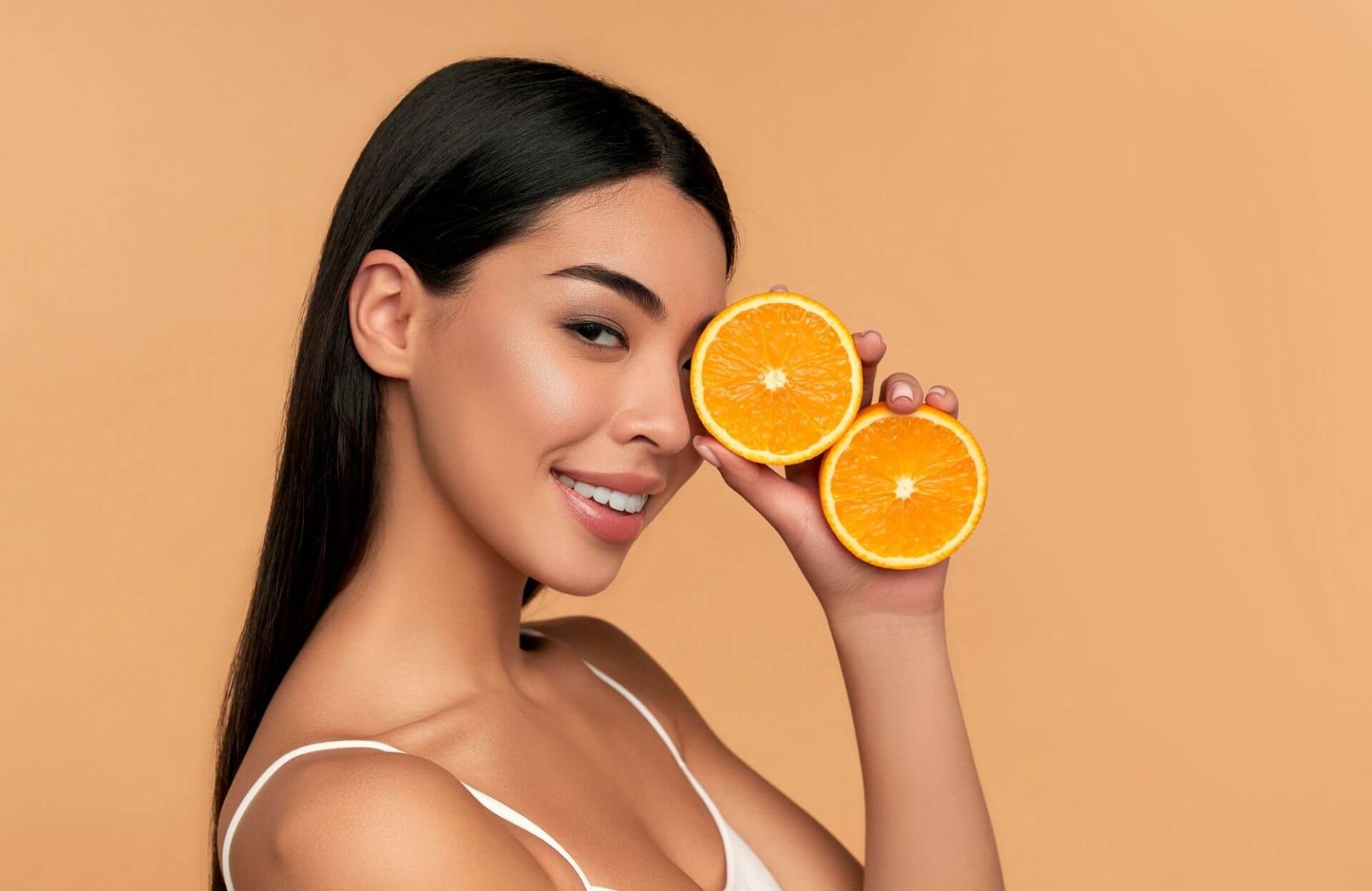 Dziewczyna trzyma przy twarzy połówki pomarańczy